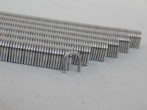 Close-up image of a hand holding a stack of shiny metal staples ready for use.