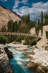 a river flowing under a bridge surrounded by mountains