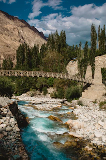 a river flowing under a bridge surrounded by mountains