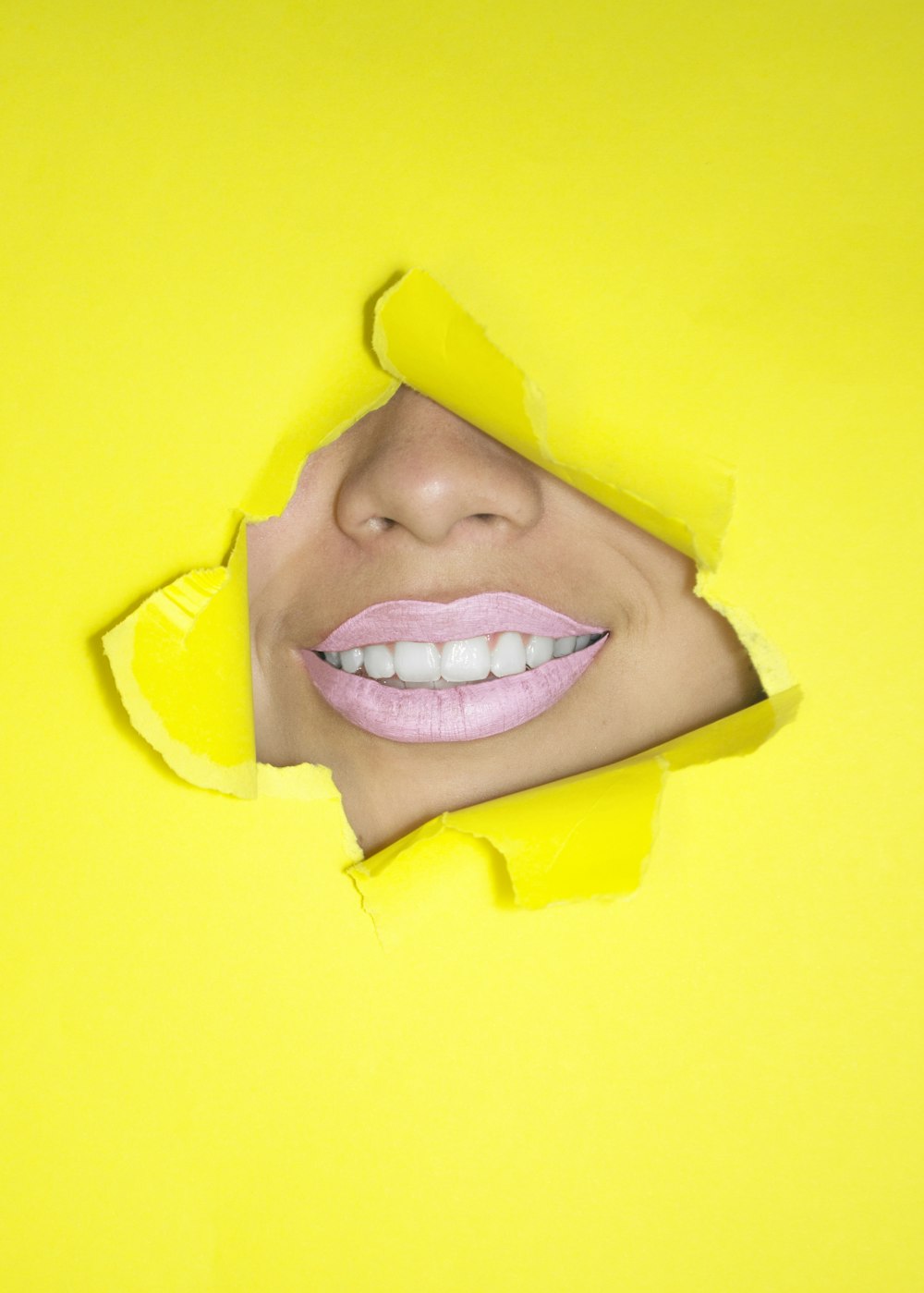 papel amarelo rasgado mostrando o nariz e os lábios da mulher