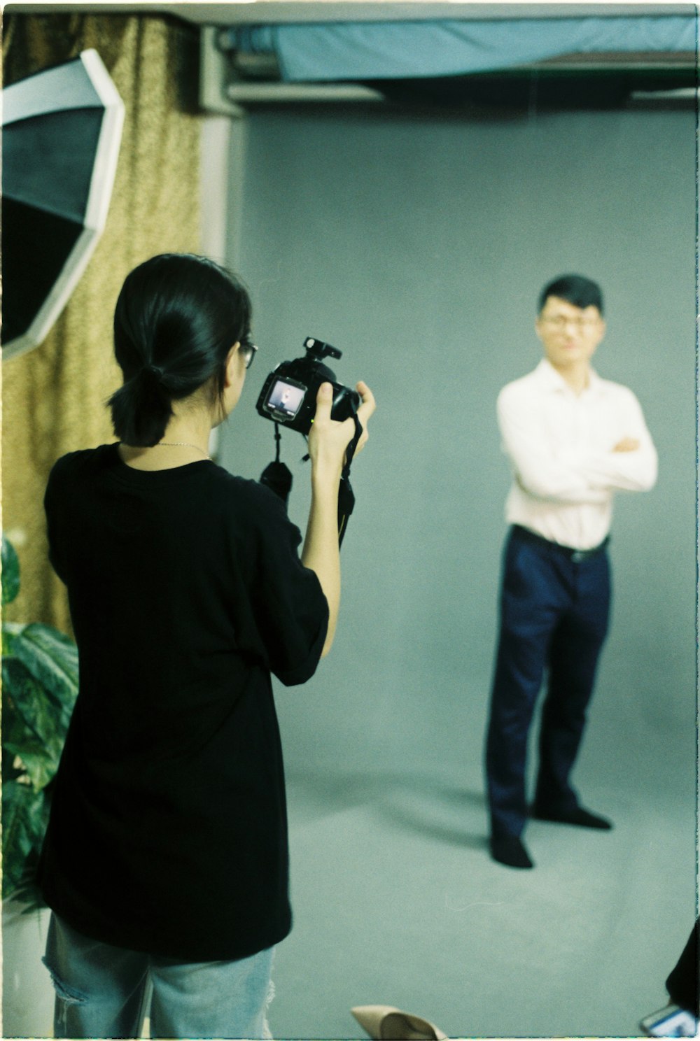 woman holding DSLR camera standing near man wearing white collared button-up long-sleeved shirt beside wall