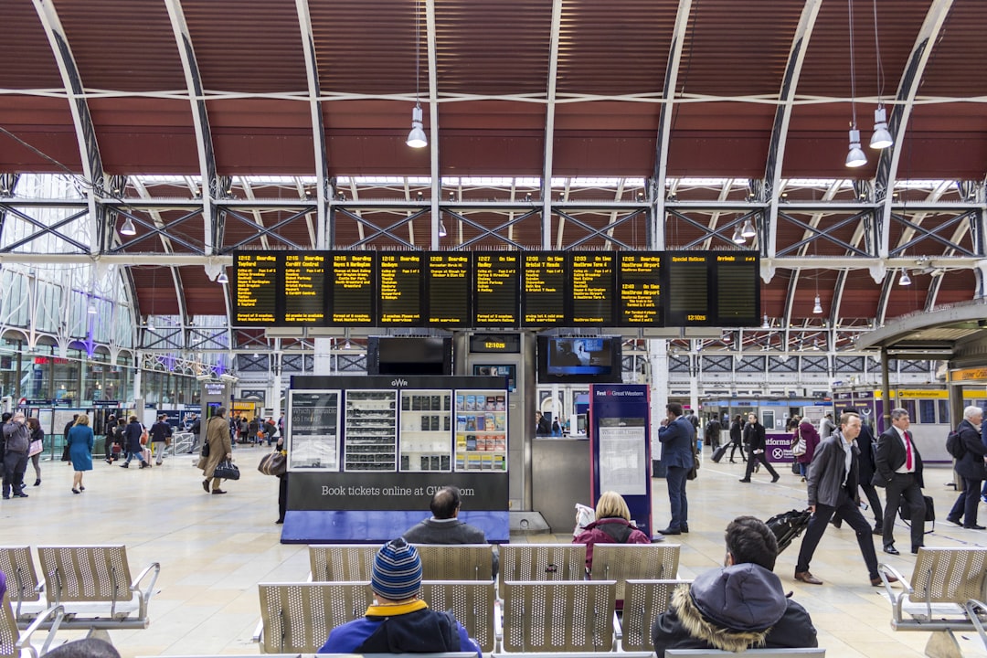 people sitting on gang chair in front of monitor, Paddington Station arrivals and departures board
