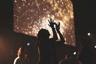 A worshipper raising hands bathed in golden light during a gospel concert.