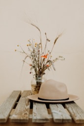 brown hat on wooden table beside flower in vase
