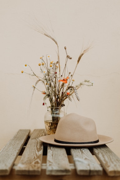 brown hat on wooden table beside flower in vase