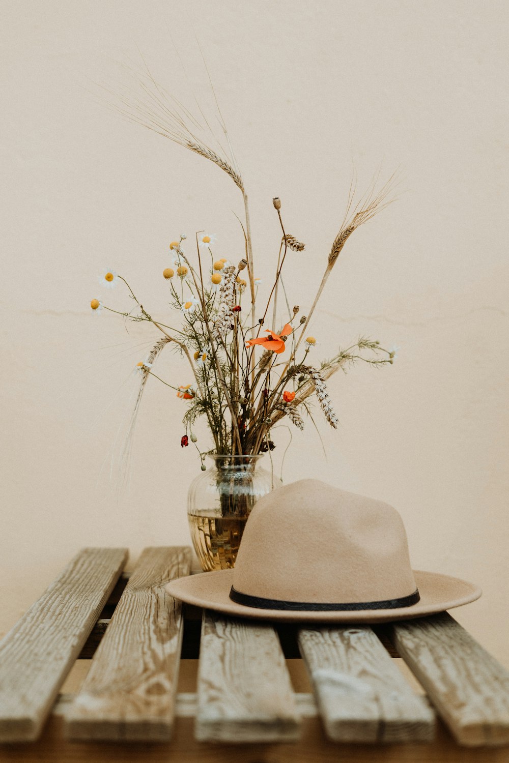 꽃병에 꽃 옆에 나무 테이블에 갈색 모자