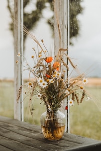 A sleek transparent glass vase holding a fresh bouquet of wildflowers on a sunlit wooden table.