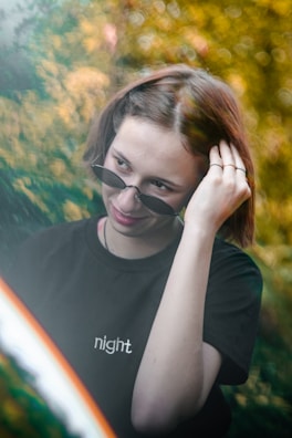 A man adjusting his obsidian black sunglasses outdoors with a blurred cityscape background.