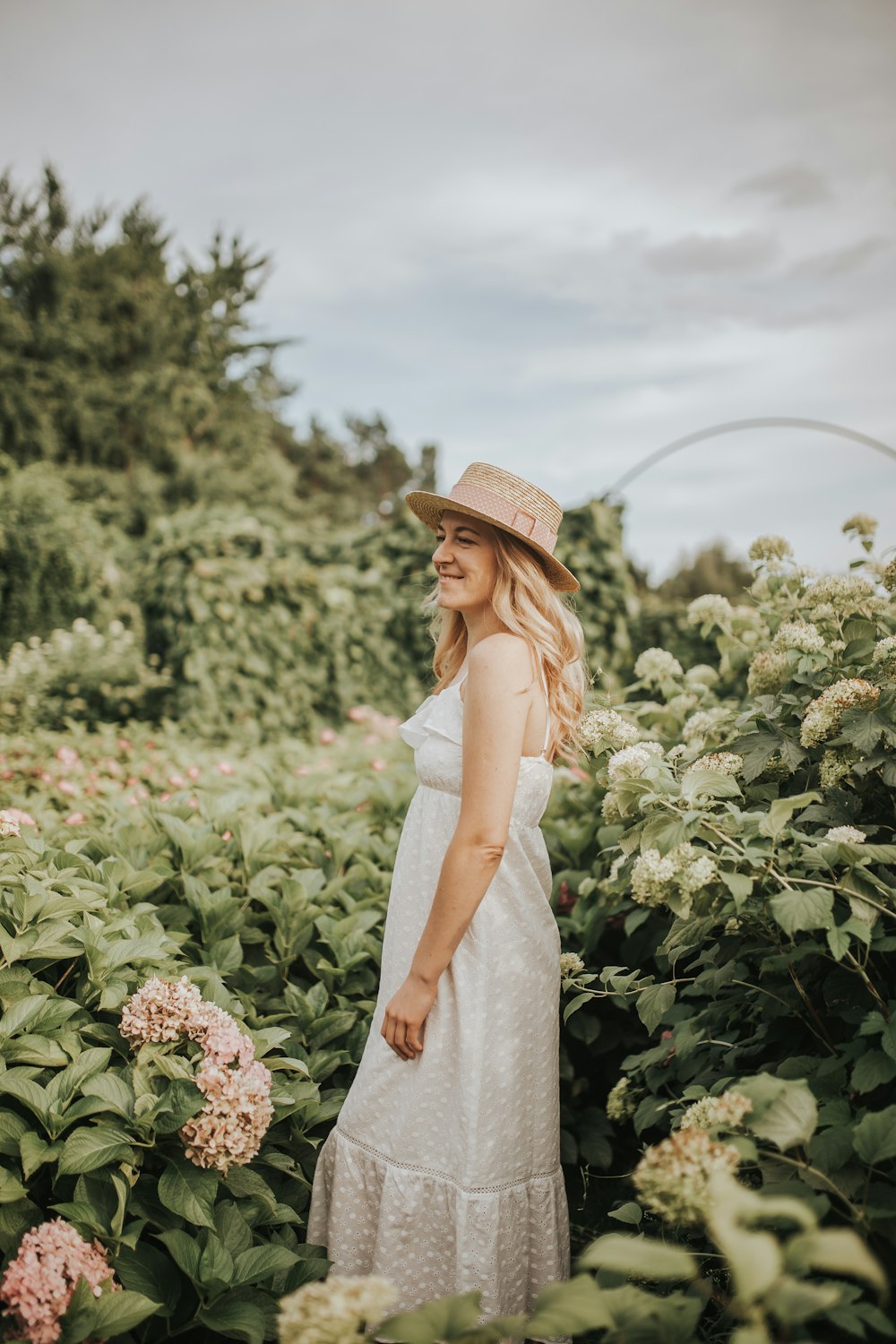 woman wearing white dress and brown hat standing beside flower field