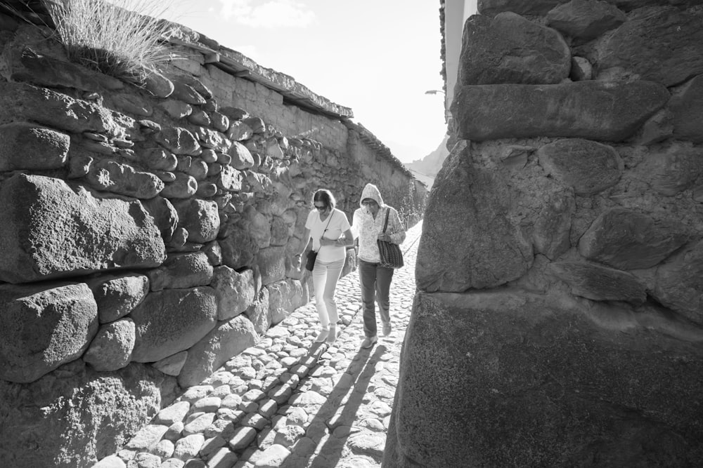 grayscale photography of two women walking along a narrow pathway