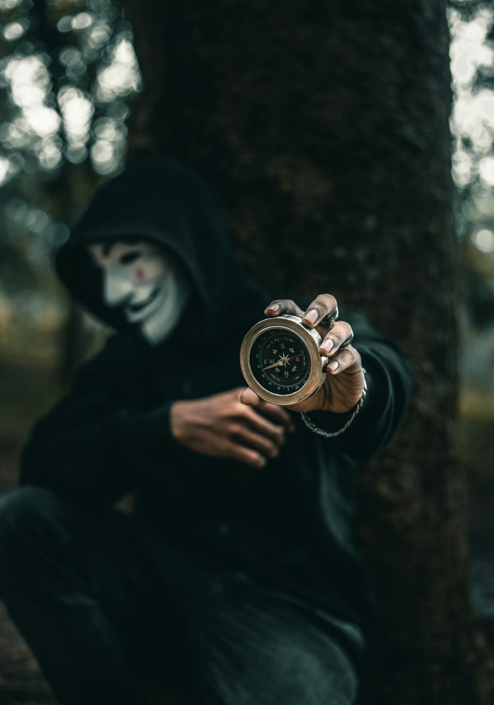 person wearing Guy Folkes mask holding round gold-colored compass