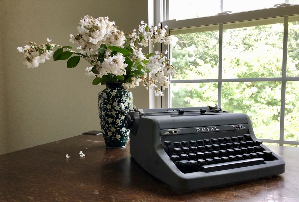 gray Royal typewriter near white flowers in vase on brown table