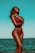 A woman stands confidently at the beach, wearing a red bikini and sunglasses. The ocean and sky create a serene backdrop, and her arms are crossed around her chest, conveying a feeling of relaxation and empowerment.