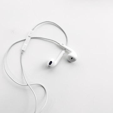 A pair of white wired earphones with a built-in control module rests on a flat, clean white surface. The earphones are neatly arranged, creating a minimalist and modern aesthetic.