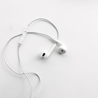 A pair of white wired earphones with a built-in control module rests on a flat, clean white surface. The earphones are neatly arranged, creating a minimalist and modern aesthetic.