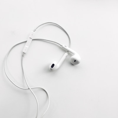 A pair of white wired earphones with a built-in control module rests on a flat, clean white surface. The earphones are neatly arranged, creating a minimalist and modern aesthetic.