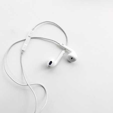 A pair of white wired earphones with a built-in control module rests on a flat, clean white surface. The earphones are neatly arranged, creating a minimalist and modern aesthetic.