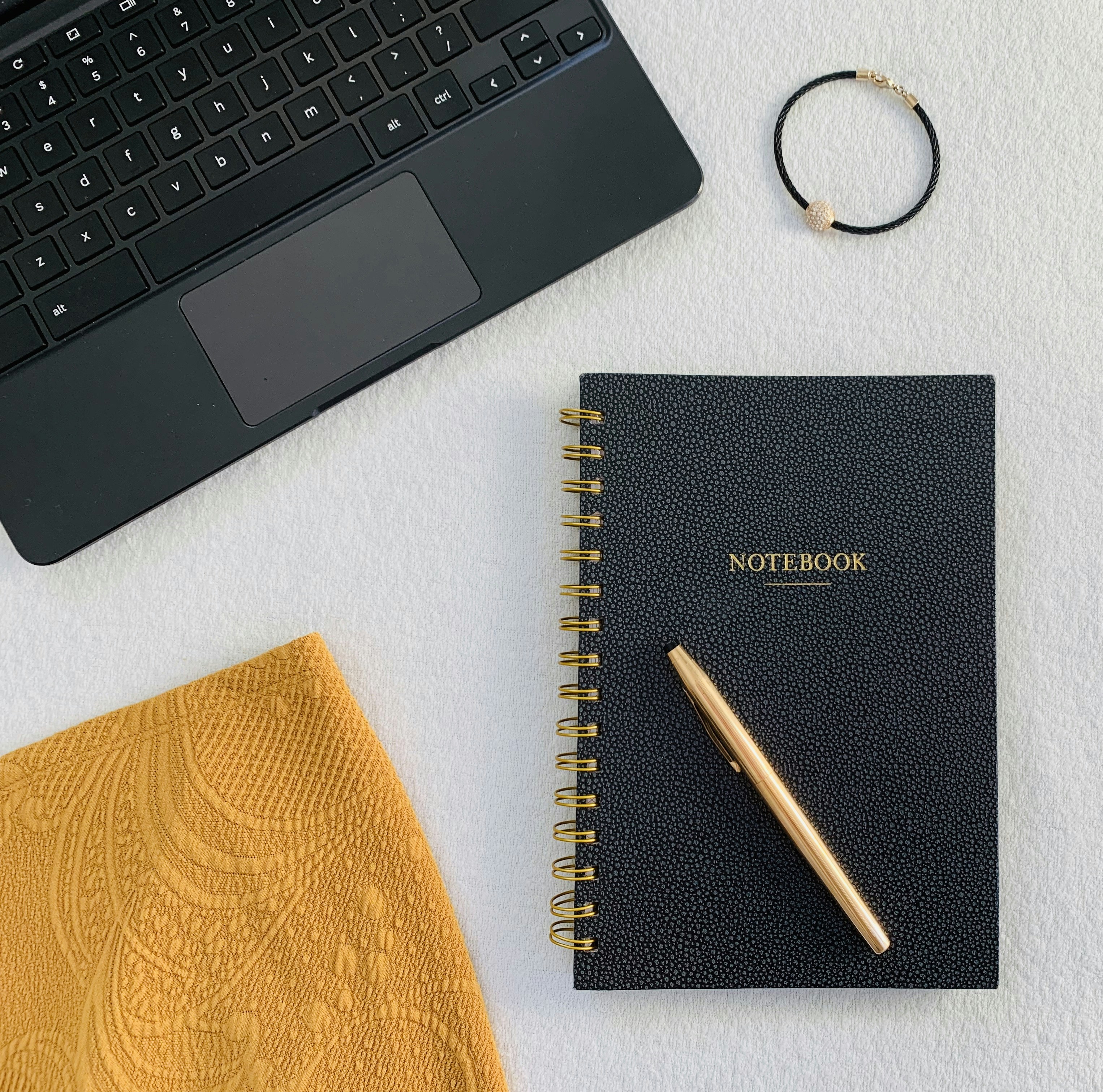 Writing workspace with laptop keyboard, black notebook with pen, and personal accessories