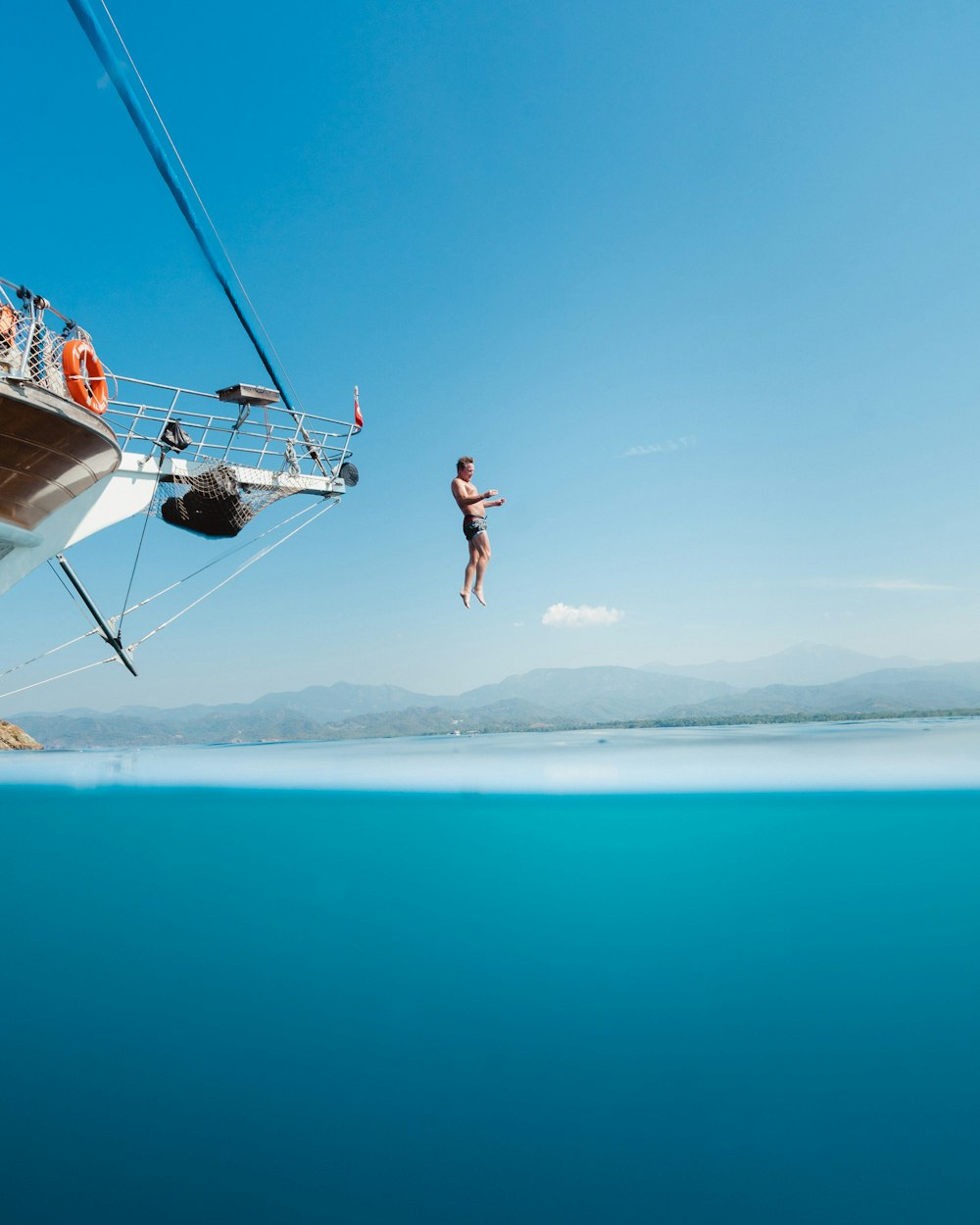 topless man jumping from boat viewing mountain during daytime