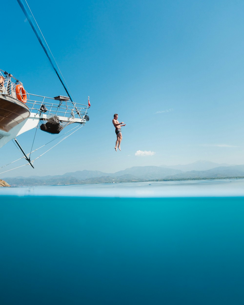 Hombre en topless saltando desde un barco viendo la montaña durante el día