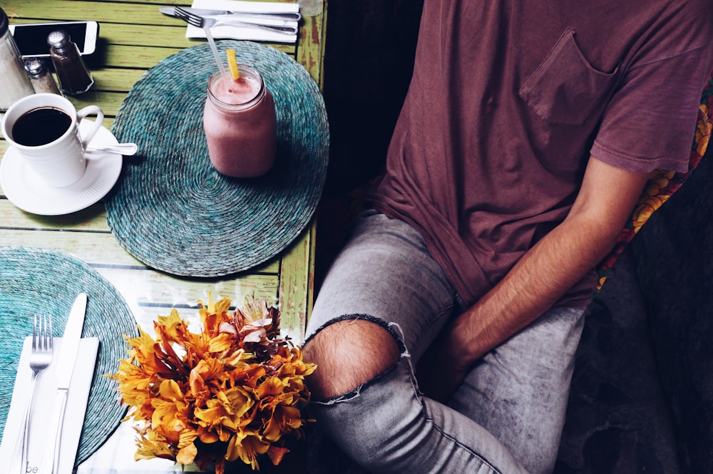 flat-lay photography of man sitting beside mug of smoothie and cup of coffee