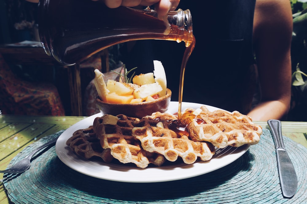 person poring syrup on waffles