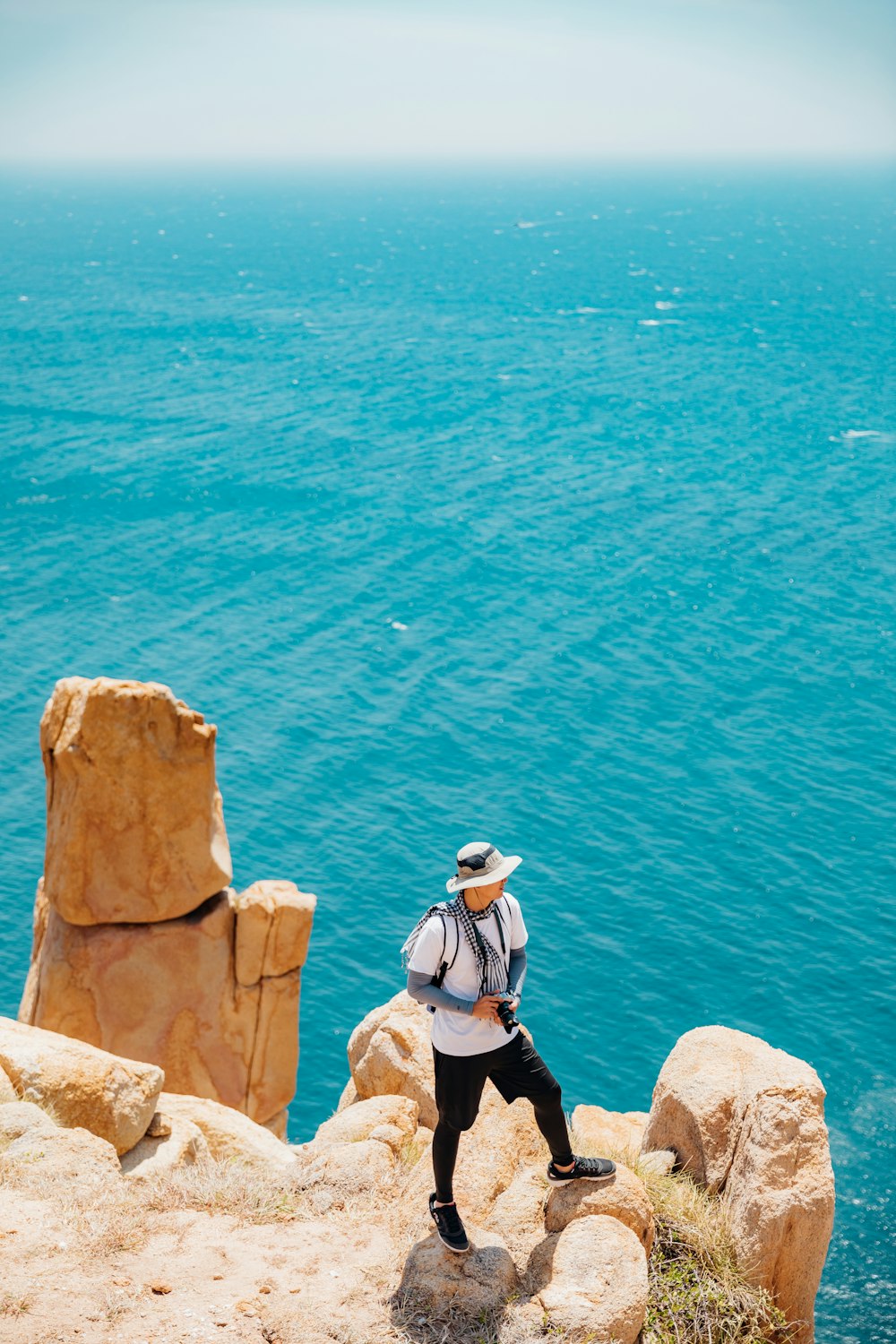 man standing on beach cliff viewing sea during daytime