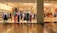 Mannequins dressed in various colorful outfits are displayed in a fashion store window. The interior is brightly lit, showcasing racks filled with neatly organized clothing items. The store has a modern, luxurious appearance with polished flooring.