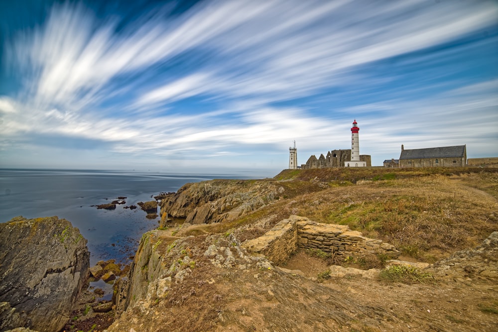 lighthouse under cloudy sky near cliff