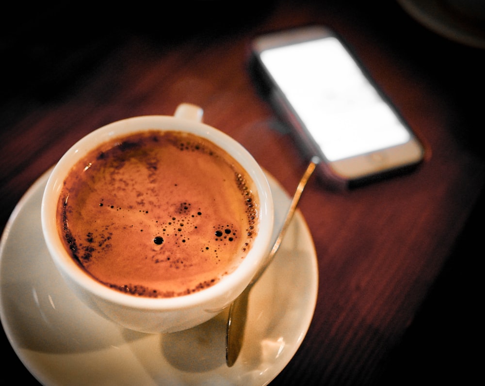 cup of coffee on saucer beside smartphone