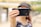 A person is holding a smartphone in front of their face, partially obscuring their features. The focus is on the phone, with a blurred background. The hand holding the phone is adorned with gold bracelets.