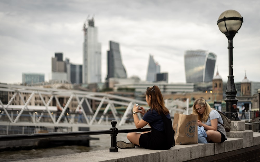 two women sitting on pavement near bridge