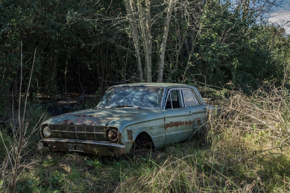 an old car sitting in the middle of a forest