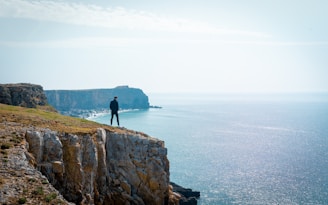 A person standing alone on a cliff edge, looking out over a vast landscape, embodying independence.