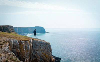 Renata standing on a cliff edge overlooking a vast ocean horizon