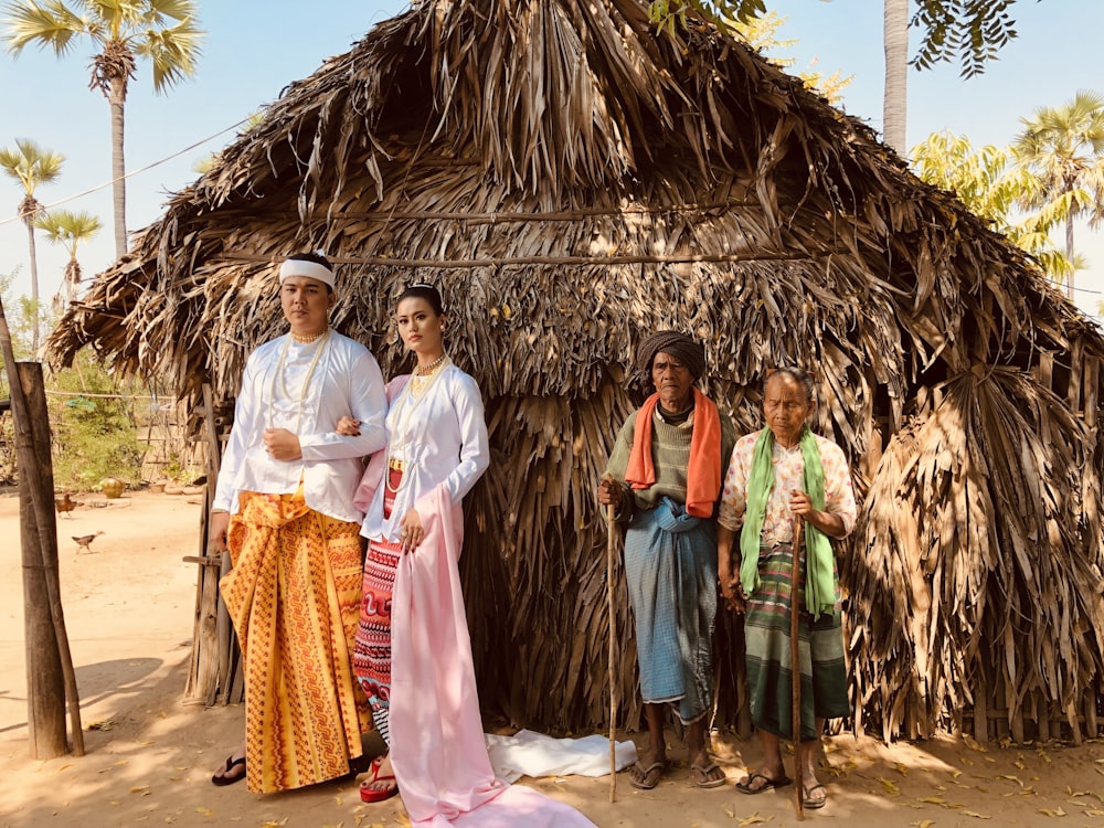 man and woman standing near another old man and woman beside straw house