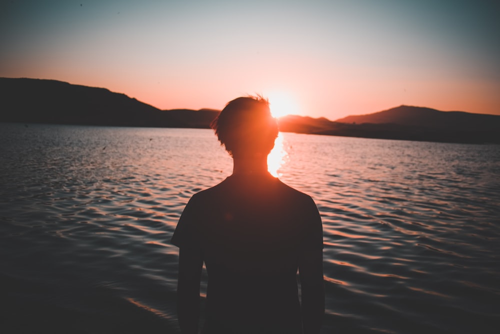 silhouette of man facing body of water