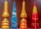 Four decorative candles with Hebrew inscriptions are displayed against a plain background. The candles vary in color and shape, including shades of orange, blue, yellow, and red. Two of the candles have a tear-shaped form, while the others are pyramid-shaped.
