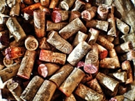 A collection of wine corks with intricate designs and text, primarily beige in color with some hints of red and brown. They are scattered in a seemingly random pile, creating a textured surface.