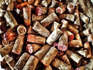 A collection of wine corks with intricate designs and text, primarily beige in color with some hints of red and brown. They are scattered in a seemingly random pile, creating a textured surface.