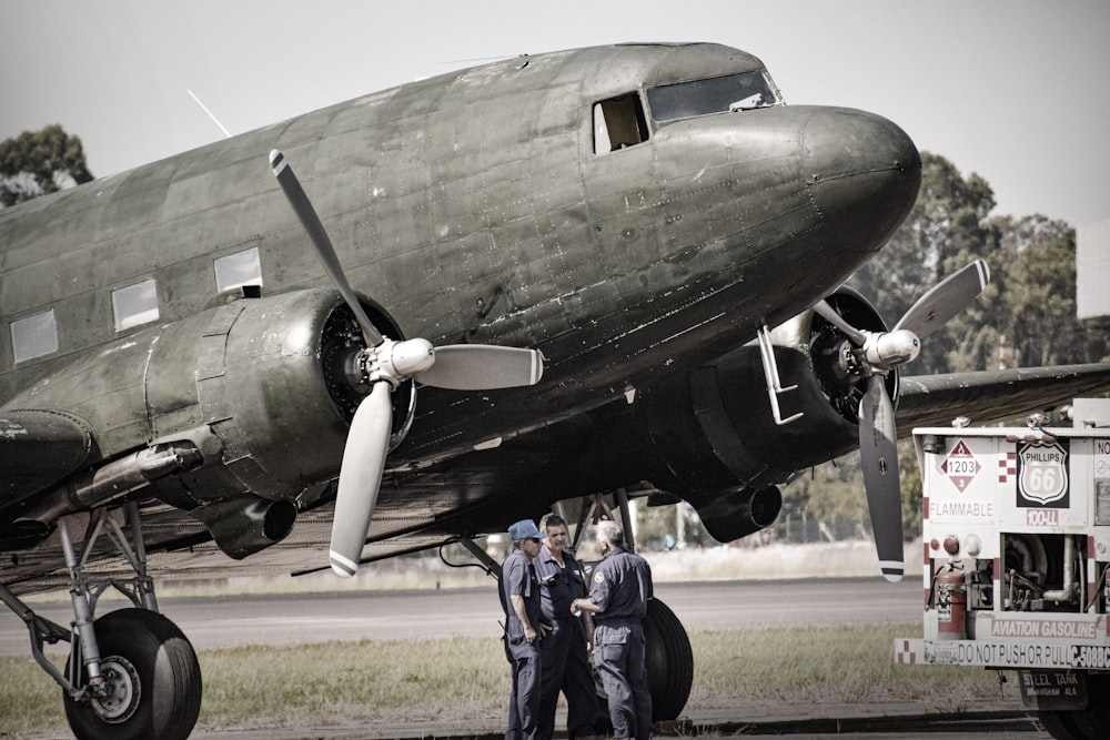 grayscale photography of three men standing beside airplane