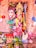A colorful and ornate statue of a Hindu goddess is adorned with intricate jewelry and a vibrant garment. The deity has a serene expression and is surrounded by decorative elements, including balloons and garlands. Various offerings and religious items are placed in front of the statue.