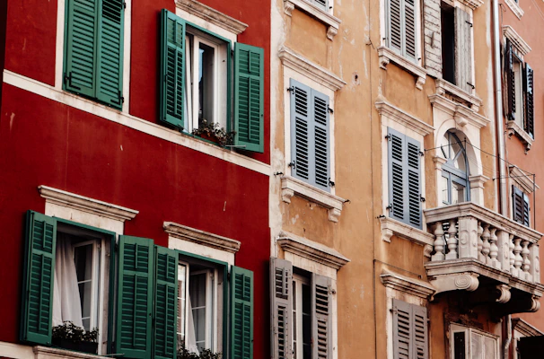Before and after shots of a freshly painted Alicante building facade with vibrant crimson and forest green accents.