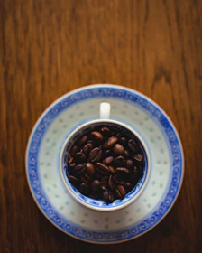 An overhead view of a coffee cup surrounded by coffee beans on a rustic wooden table.