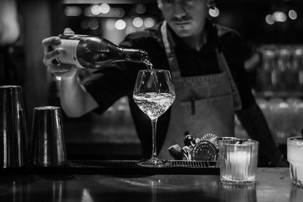 grayscale photo of bartender pouring liquid in wine glass