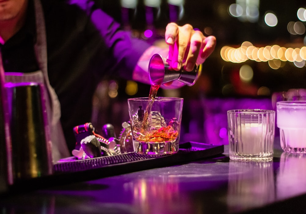 person pouring liquor in clear drinking glass