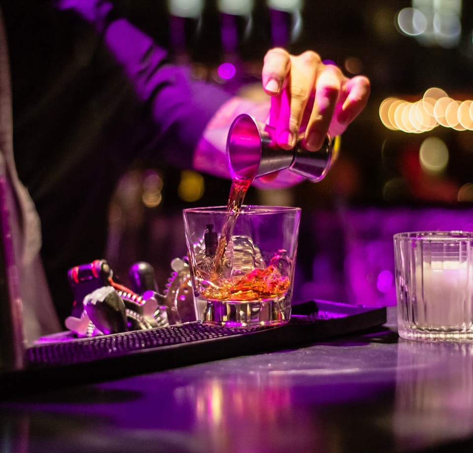 person pouring liquor in clear drinking glass