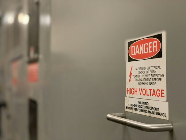 Señal de peligro de alta tensión colocada sobre un tablero eléctrico industrial, contexto del marketing para empresas de seguridad industrial