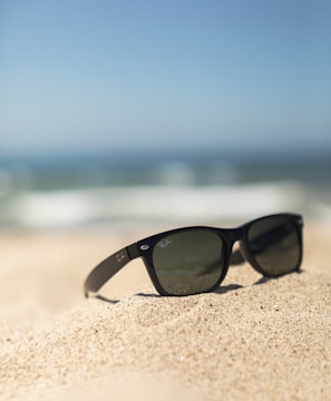 black wayfarer-style sunglasses on sand