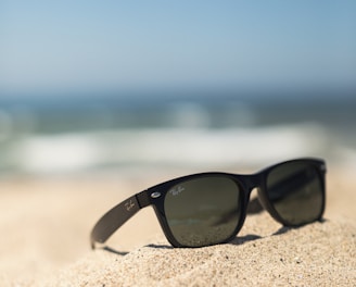 black wayfarer-style sunglasses on sand